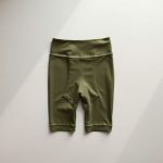 Flat lay of olive green black legging with pockets, seamfree bike shorts folded neatly on a neutral surface.